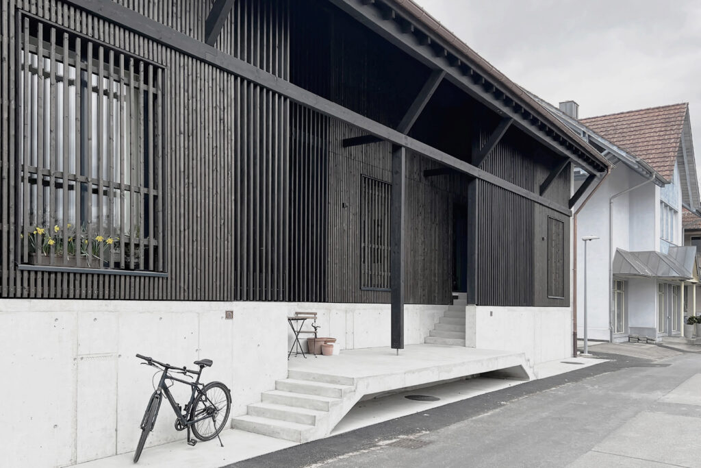 Ansicht der Remise, Alle Gebäude haben zum Hochwasserschutz einen Betonsockel der sich als Teil der Fassadengestaltung sichtbar abzeichnet.