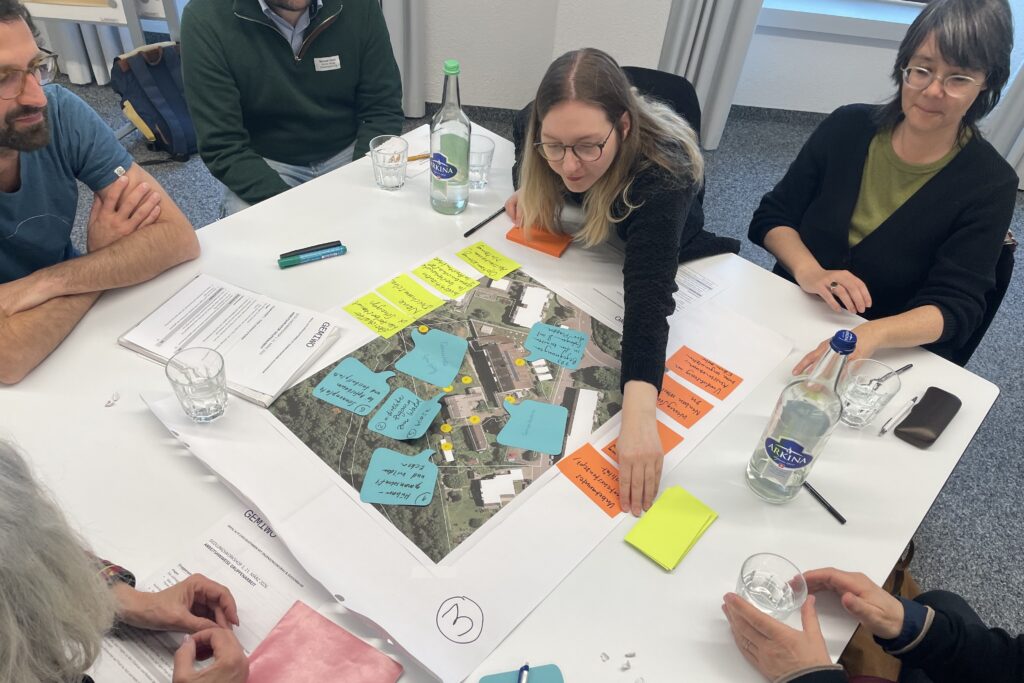 Eine Frau lehnt sich über einen Tisch und klebt einen Notizzettel auf einen Plan.