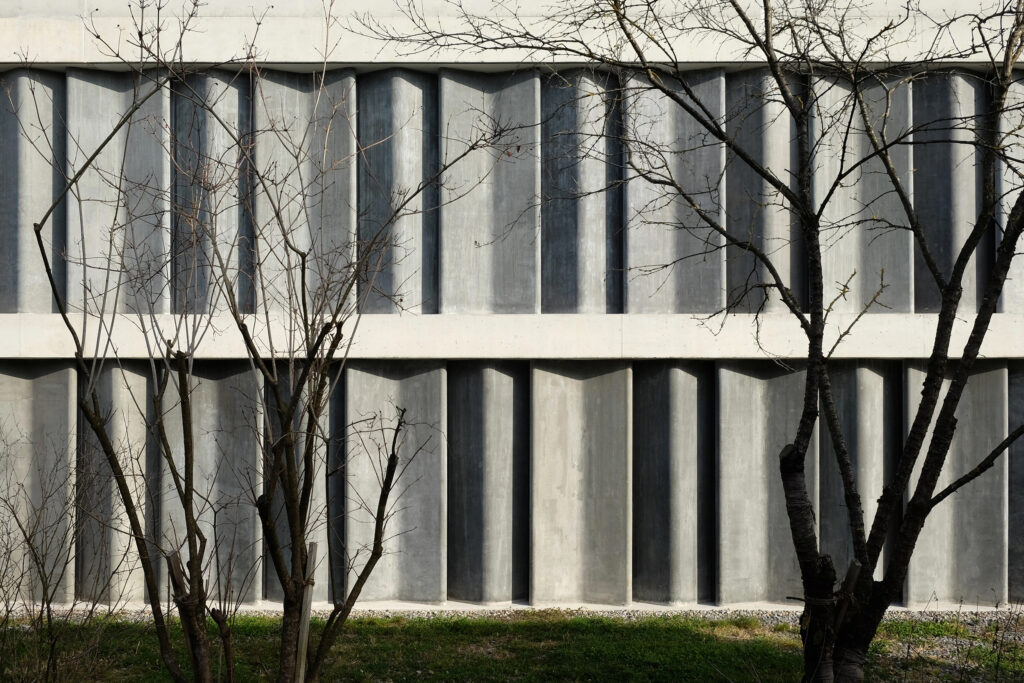 Ansicht der Fassade, V-förmige Betonelemente sorgen für den Witterungsschutz, Licht fällt durch Spalten dezent in den Innenraum